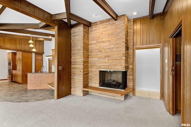 unfurnished living room with beamed ceiling, light colored carpet, a stone fireplace, and wood walls