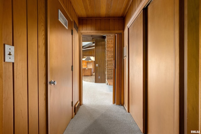 hallway with light carpet, wood ceiling, and wood walls