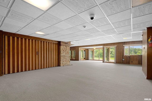 interior space featuring carpet flooring, a drop ceiling, and wood walls