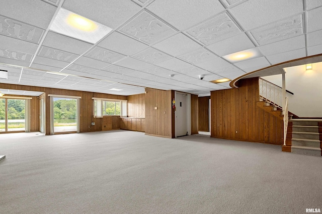 unfurnished living room featuring light carpet, a drop ceiling, and wooden walls