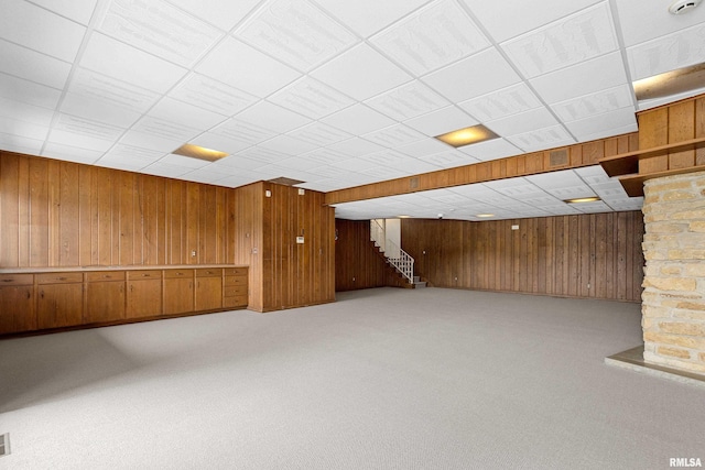 basement featuring a drop ceiling, carpet floors, and wood walls