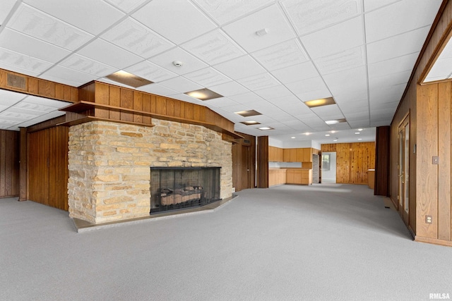 unfurnished living room with carpet floors, a paneled ceiling, a fireplace, and wooden walls