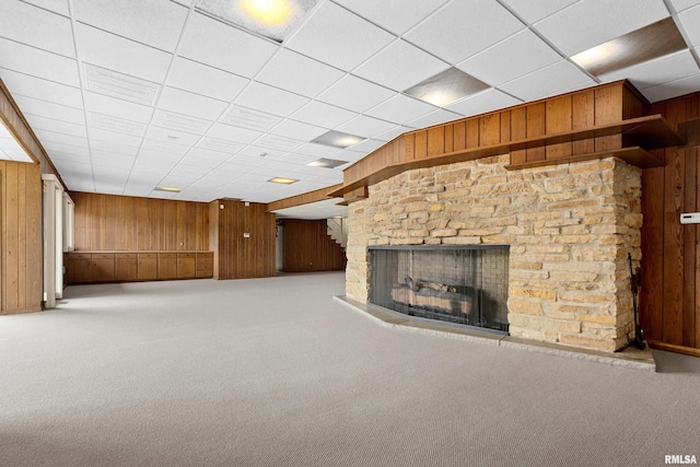 unfurnished living room with a multi sided fireplace, wooden walls, a paneled ceiling, and carpet flooring