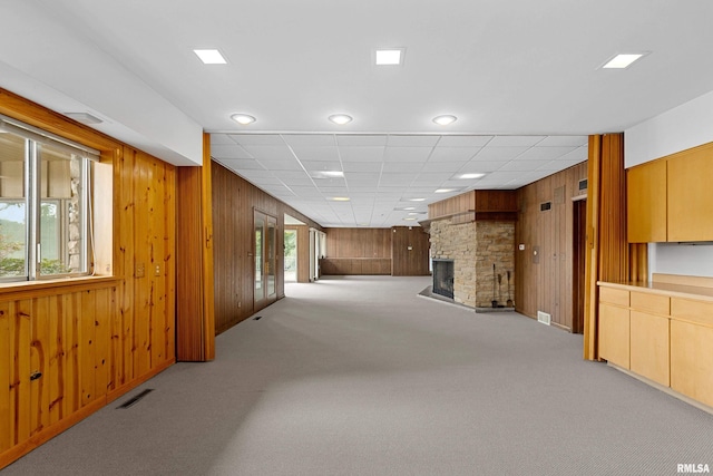 living room featuring light colored carpet, a fireplace, wooden walls, and a drop ceiling