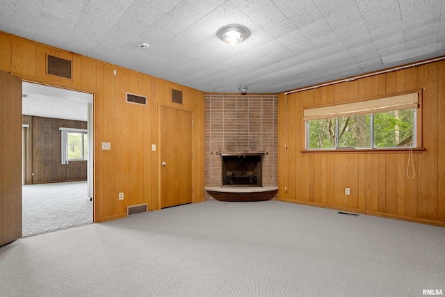 unfurnished living room with a brick fireplace, plenty of natural light, wood walls, and carpet