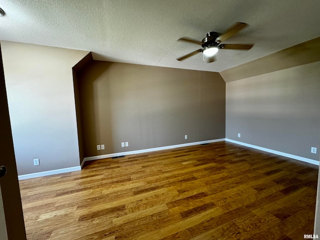 empty room with ceiling fan, hardwood / wood-style flooring, a textured ceiling, and vaulted ceiling