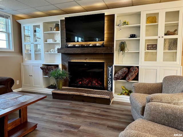 living room with a large fireplace, hardwood / wood-style flooring, and a drop ceiling