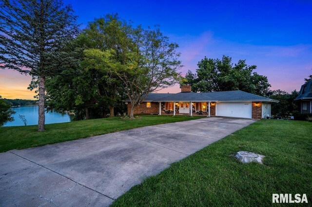 ranch-style home featuring a water view, a lawn, and a garage