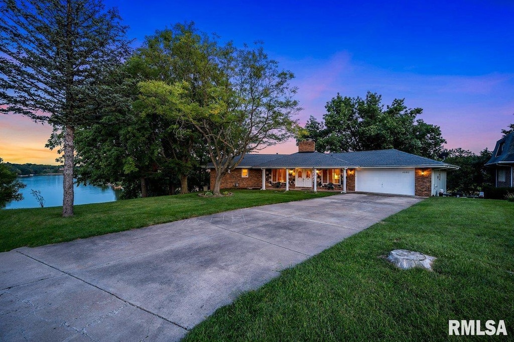 ranch-style home featuring driveway, a water view, an attached garage, and a front yard