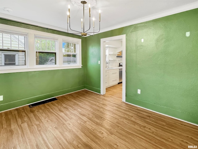 unfurnished dining area featuring ornamental molding, sink, light wood-type flooring, and a chandelier