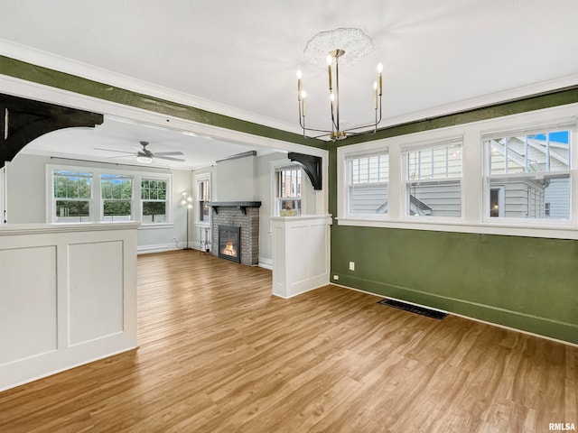 unfurnished living room with light wood-type flooring, ceiling fan with notable chandelier, and crown molding