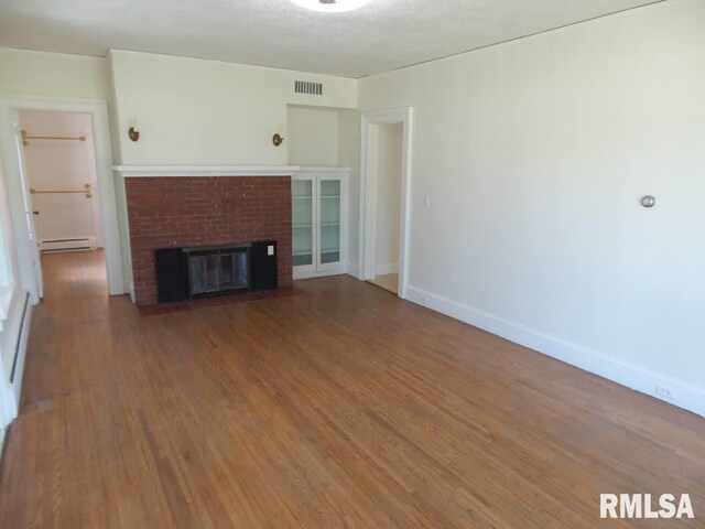 unfurnished living room featuring a fireplace, hardwood / wood-style floors, and a baseboard heating unit