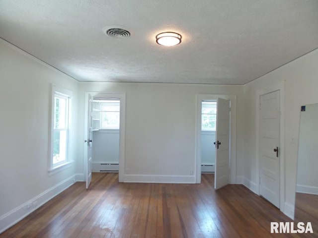 unfurnished bedroom with dark wood-type flooring, a textured ceiling, and a baseboard heating unit