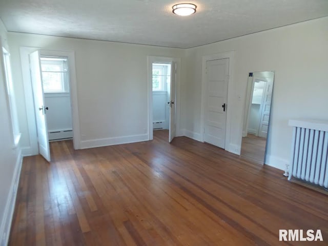 spare room featuring baseboard heating, dark hardwood / wood-style flooring, and plenty of natural light