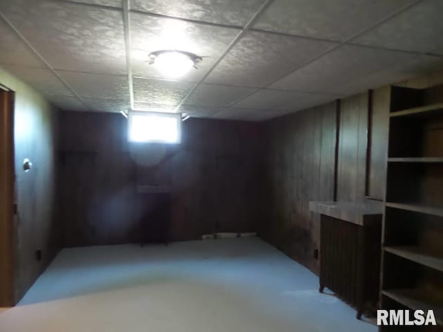 basement featuring wood walls and a drop ceiling