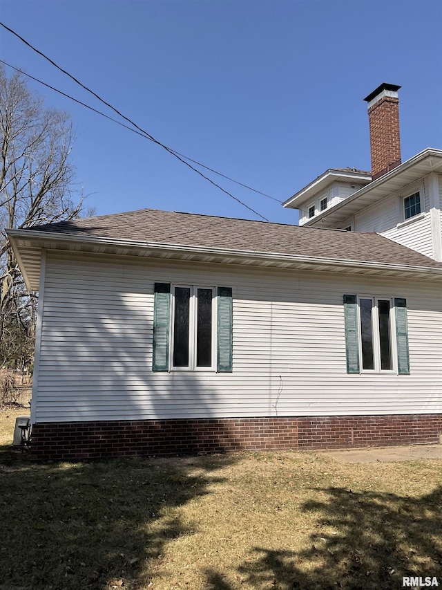 view of side of home featuring a shingled roof and a yard