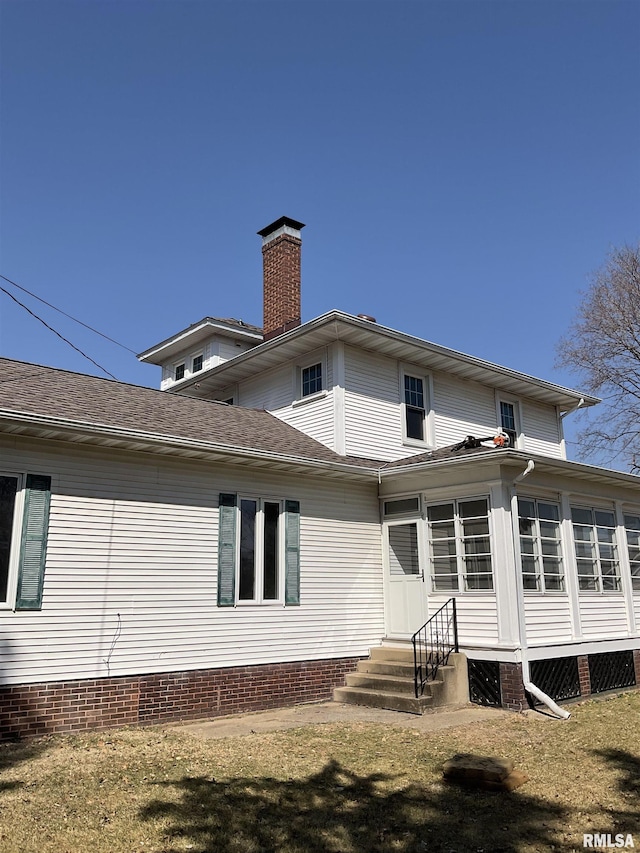 rear view of property with a yard, entry steps, and a chimney