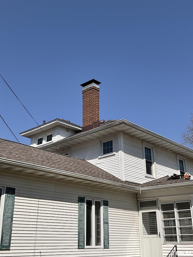 view of side of home featuring a chimney and a shingled roof