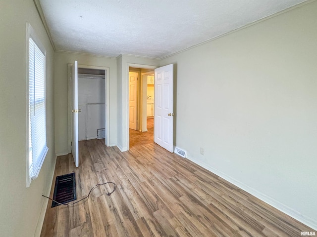 unfurnished bedroom with a textured ceiling, light hardwood / wood-style flooring, multiple windows, and a closet