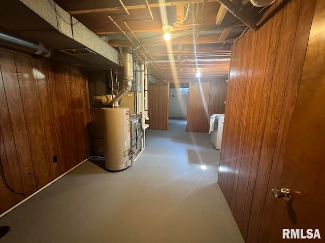 basement with water heater, wood walls, and washing machine and dryer