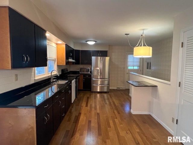 kitchen with sink, kitchen peninsula, decorative light fixtures, stainless steel appliances, and hardwood / wood-style floors