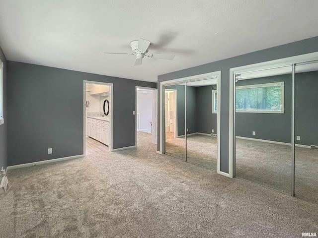 unfurnished bedroom featuring two closets, connected bathroom, ceiling fan, and light colored carpet