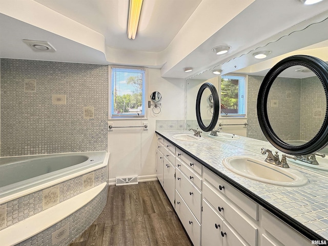 bathroom featuring hardwood / wood-style flooring, plenty of natural light, tiled bath, and vanity