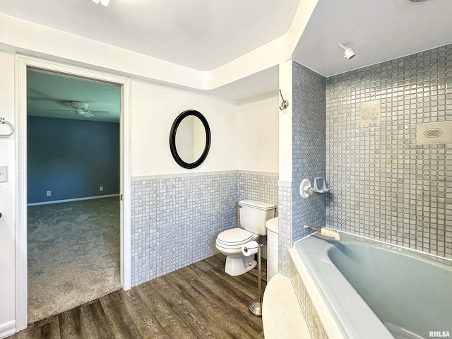 bathroom featuring tiled shower / bath combo, tile walls, toilet, and wood-type flooring