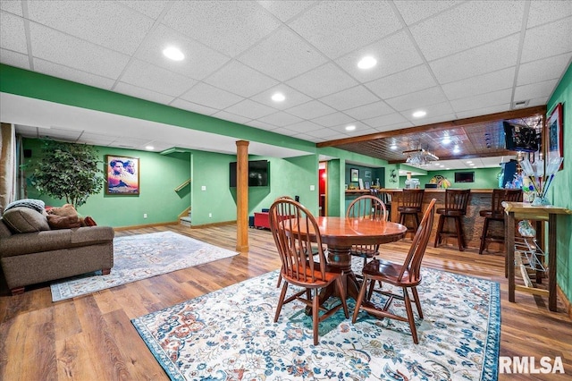 dining area with wood-type flooring, bar, and a drop ceiling