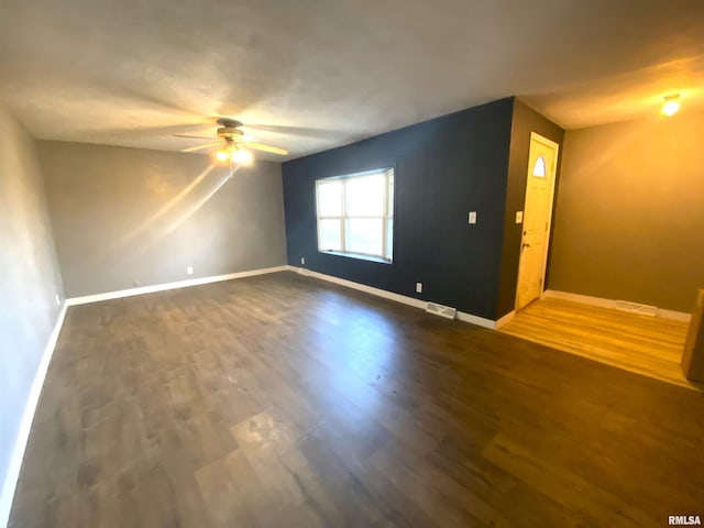 empty room with a ceiling fan, dark wood finished floors, and baseboards