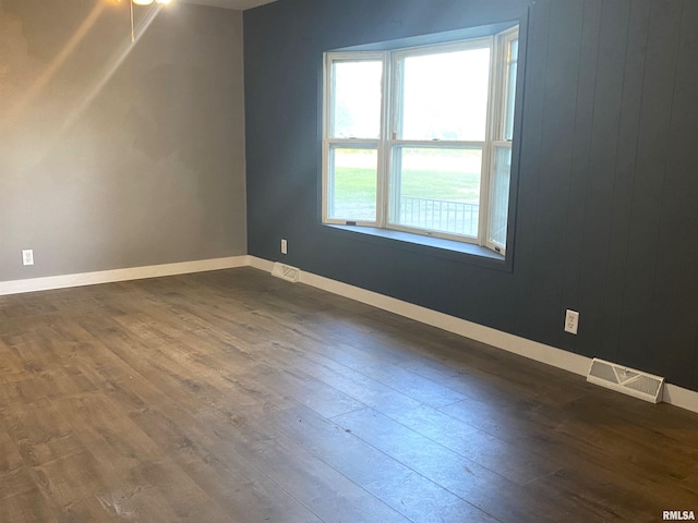 spare room with dark wood-style floors, visible vents, and baseboards