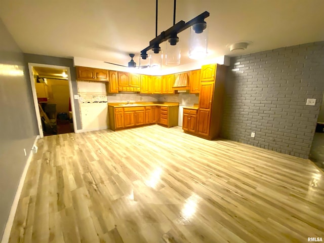 kitchen with light countertops, light wood-style floors, brown cabinetry, a sink, and brick wall