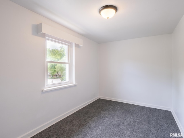 spare room with baseboards and dark carpet