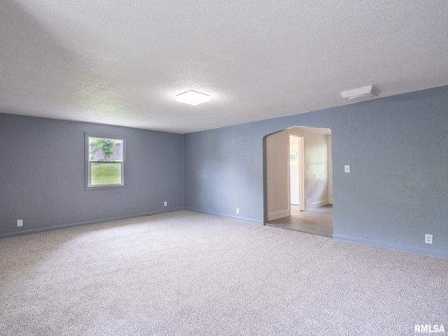 carpeted spare room with arched walkways, a textured ceiling, and baseboards