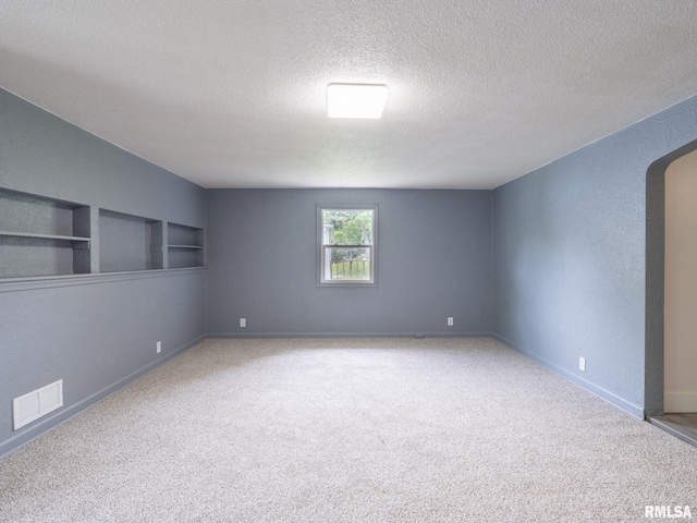 spare room featuring built in shelves, arched walkways, visible vents, and carpet floors