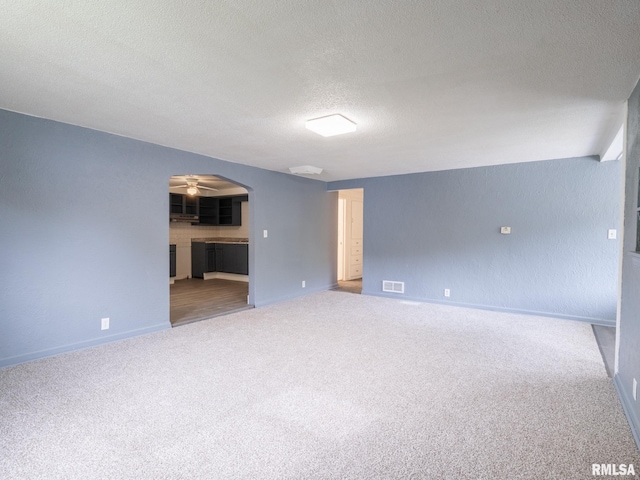 empty room with visible vents, ceiling fan, carpet floors, arched walkways, and a textured ceiling