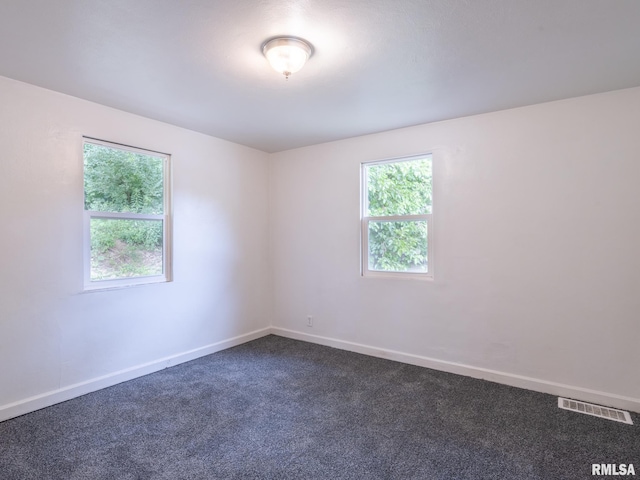 spare room featuring visible vents, baseboards, and dark colored carpet