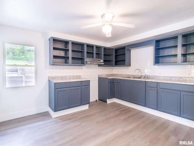 kitchen featuring open shelves, light wood-type flooring, decorative backsplash, and a sink