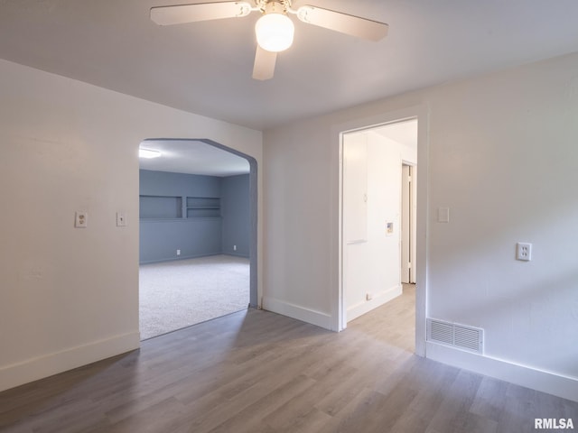 empty room featuring visible vents, arched walkways, baseboards, and wood finished floors