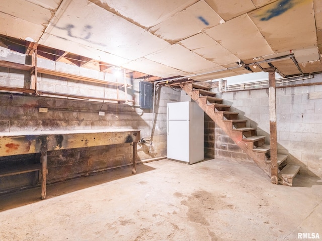 unfinished basement with electric panel, stairway, and freestanding refrigerator