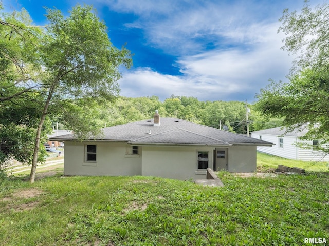 back of house featuring stucco siding, a lawn, a chimney, and a shingled roof