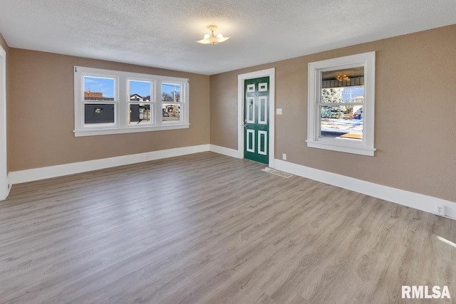 unfurnished room with light wood-type flooring and a textured ceiling