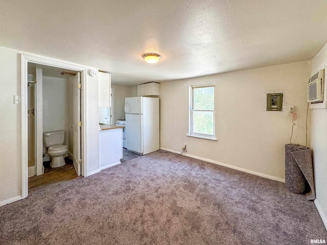 unfurnished bedroom featuring ensuite bathroom, an AC wall unit, a textured ceiling, carpet, and white refrigerator