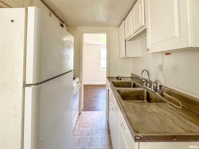 kitchen featuring light hardwood / wood-style floors, sink, white cabinets, a textured ceiling, and white appliances