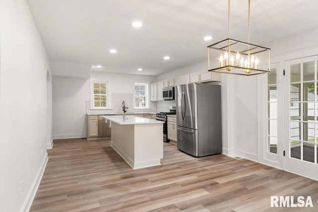 kitchen featuring pendant lighting, white cabinetry, stainless steel appliances, a kitchen island, and light wood-type flooring