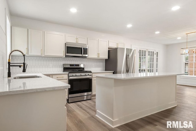 kitchen with sink, stainless steel appliances, light stone counters, white cabinets, and decorative light fixtures