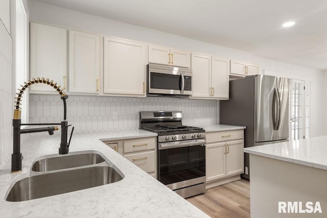 kitchen featuring sink, light hardwood / wood-style flooring, stainless steel appliances, light stone countertops, and decorative backsplash