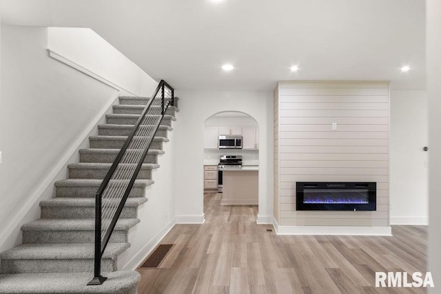 stairs featuring a glass covered fireplace, recessed lighting, visible vents, and wood finished floors