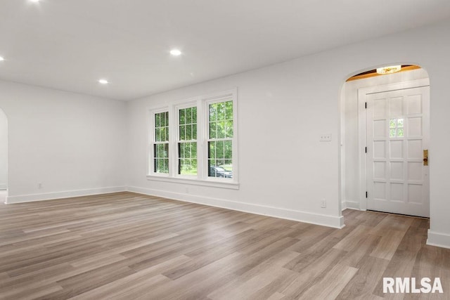 spare room with arched walkways, baseboards, and light wood-type flooring