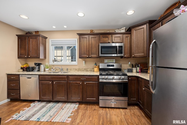 kitchen featuring light stone countertops, sink, appliances with stainless steel finishes, and light hardwood / wood-style floors